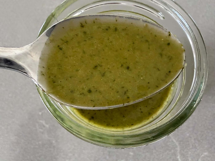 A metal spoon with cilantro lime vinaigrette held above a glass jar of cilantro lime vinaigrette.