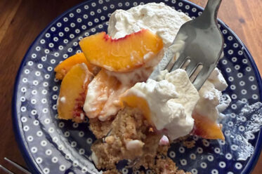 A serving of Fresh Peach dessert with a fork inserted diagonally from the upper right on a dark blue plate with white polka dots.