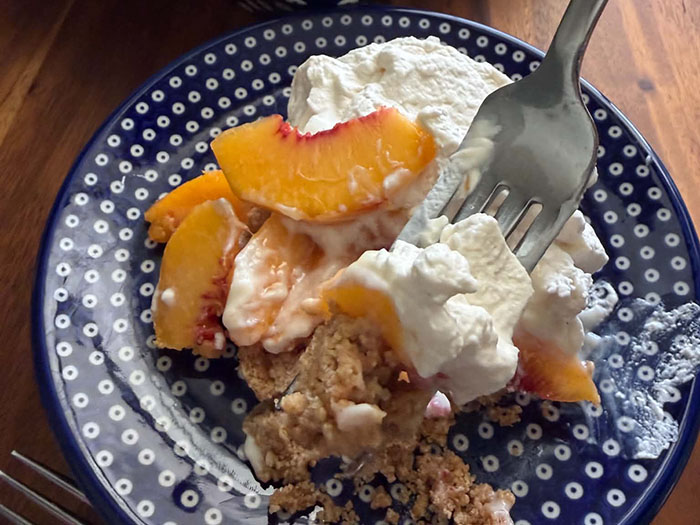 A serving of Fresh Peach dessert with a fork inserted diagonally from the upper right on a dark blue plate with white polka dots.