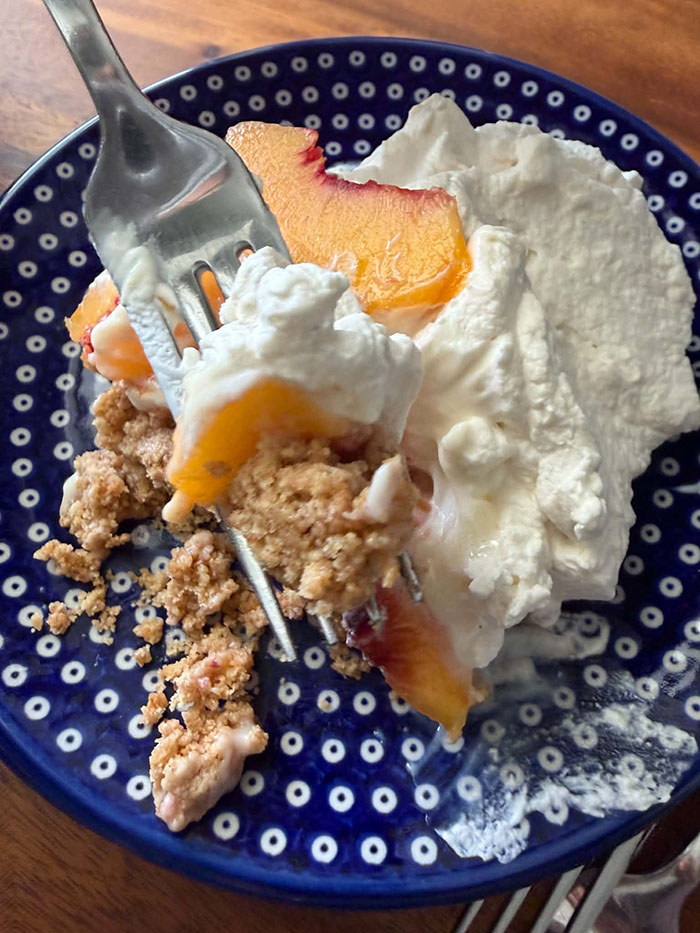 A small dark blue and white polka-dotted plate with a scoop of peach dessert with a fork held above with a bite of the peach dessert.