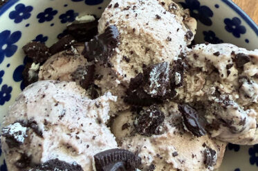 A white bowl with dark blue flowers with several scoops of Oreo ice cream with Oreo cookie pieces sprinkled on top. Several broken Oreo cookies surround the bowl at the top.