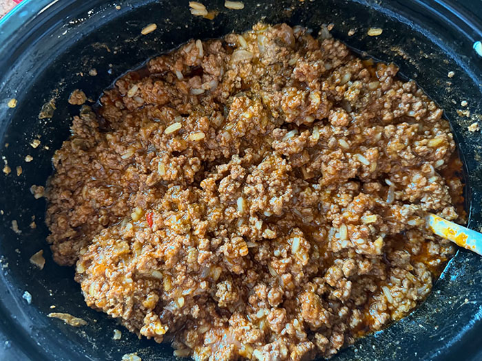 A crockpot filled with sloppy joe mixture with a serving spoon inserted diagonally from the bottom right.