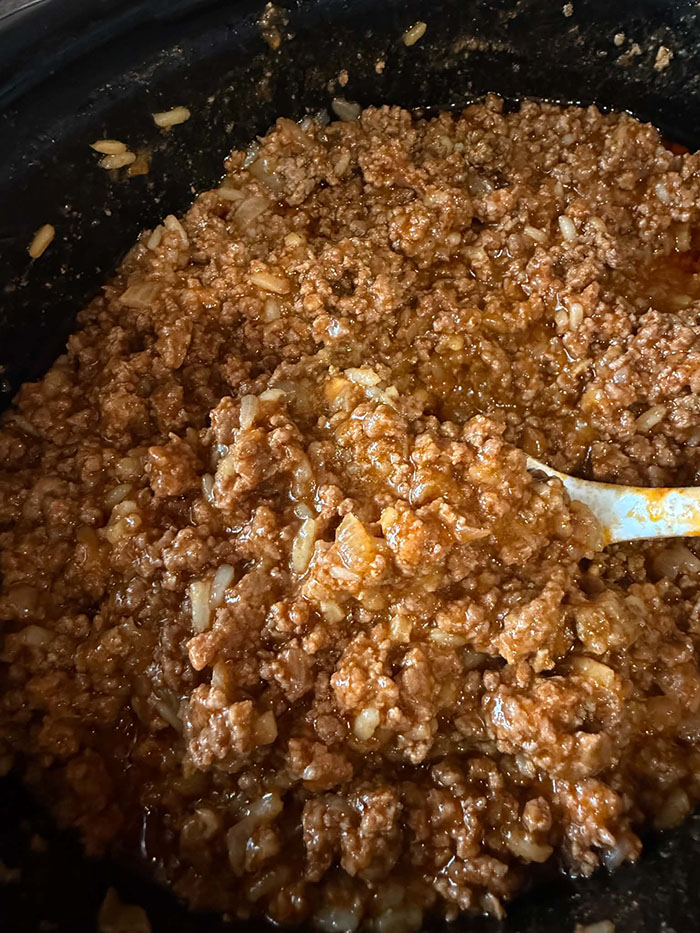 A slow cooker full of sloppy joe filling with a serving spoon inserted from the right.