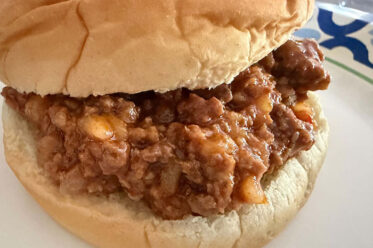 A hamburger bun filled with sloppy joe mixture on a paper plate.