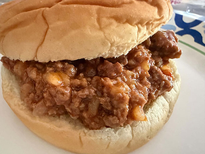 A hamburger bun filled with sloppy joe mixture on a paper plate.