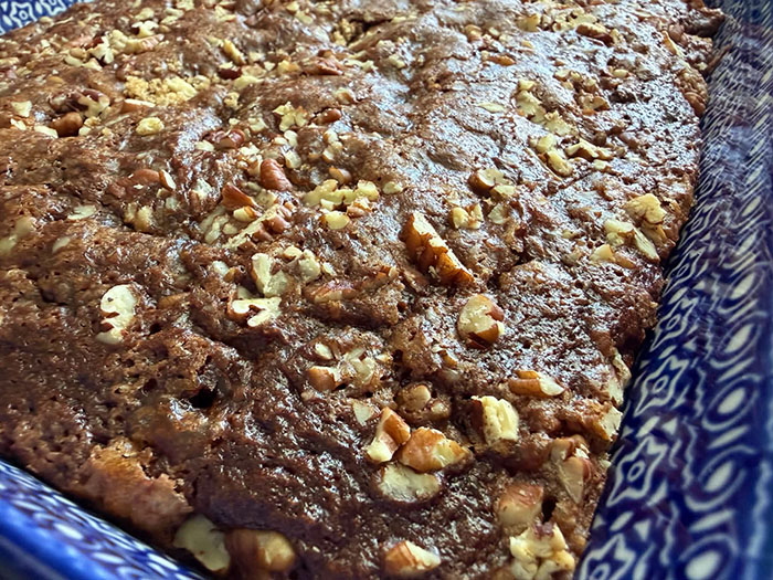 A closeup picture of a partial picture of a dark blue 9x13 baking dish of zucchini chocolate cake with pecan streusel.