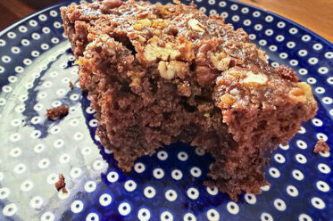 A slice of chocolate zucchini cake with pecan streusel with a bite taken out on a small dark blue plate with polka dots.