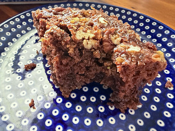 A slice of chocolate zucchini cake with pecan streusel with a bite taken out on a small dark blue plate with polka dots.
